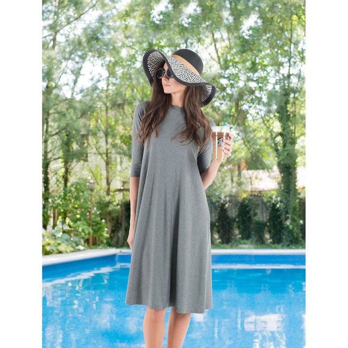 Woman in a gray dress and sun hat by a pool with trees in the background